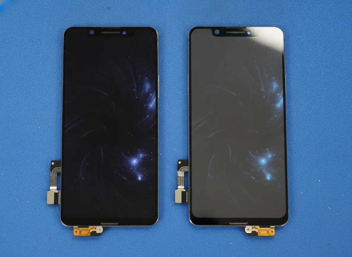 Deux écrans de smartphone de remplacement posés côte à côte sur un tapis antistatique, l’un affichant des noirs plus profonds